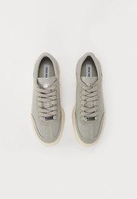 Adidași gri din suede și piele cu șireturi, cu talpă bej, văzuți din sus, eticheta "Steve Madden" pe limbă și pe eticheta șiretului.