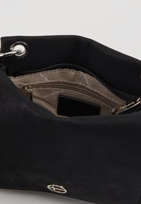 Borsa in suede nera con tasca interna con cerniera e rivestimento beige. Presenta un logo argentato e una texture liscia. Si apre ampiamente per un facile accesso.