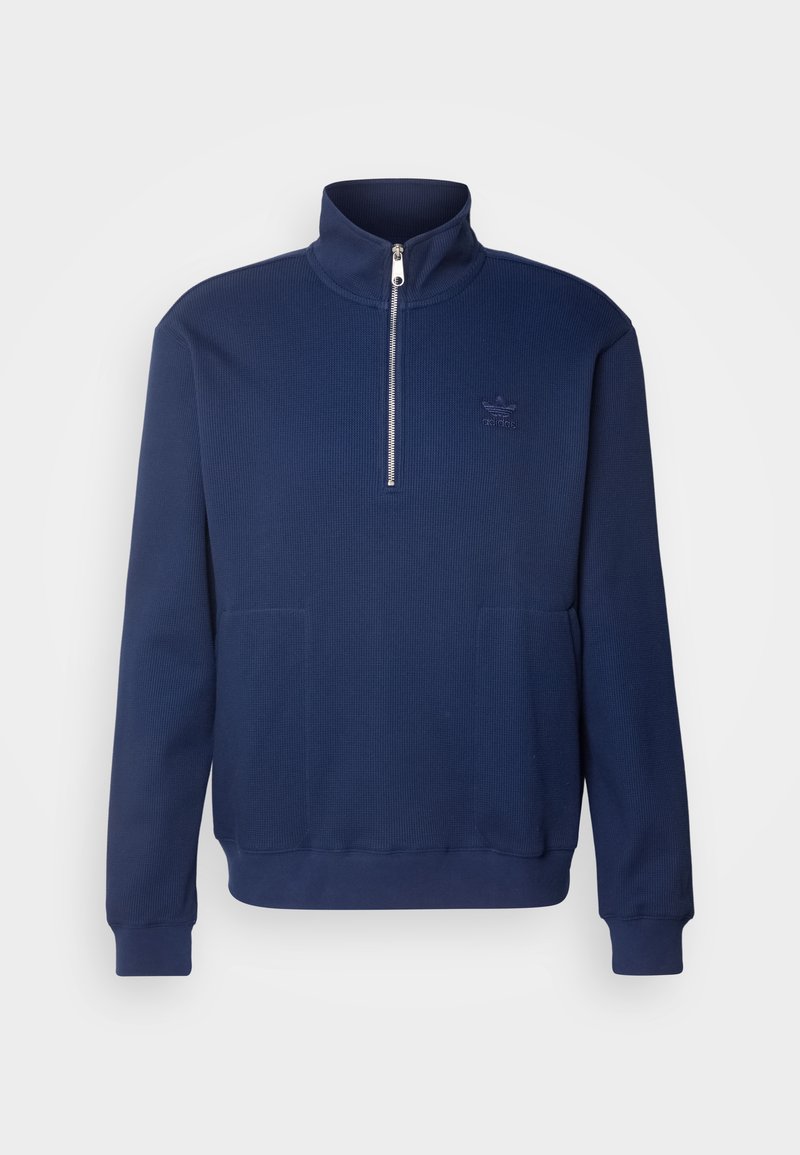 Granatowy sweatshirt z wysokim kołnierzem, zamek błyskawiczny do połowy, prążkowana faktura materiału i dwie przednie kieszenie. Zawiera subtelne logo na klatce piersiowej.