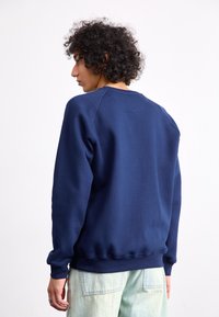 Mørkeblå sweatshirt med rund hals, ribbede mansjetter og liv. Blødt stof med en let struktureret overflade. Tætsiddende pasform.