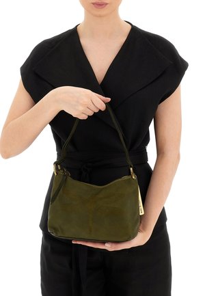 Borsa a tracolla in pelle verde oliva con motivo di libellule, chiusura con zip e manico corto, tenuta in mano contro un outfit nero.