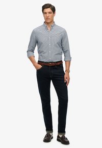 Camisa de cuadros azul y blanca de botones, jeans oscuros, cinturón trenzado marrón y mocasines marrones con calcetines blancos. Texturas suaves y ajuste entallado.