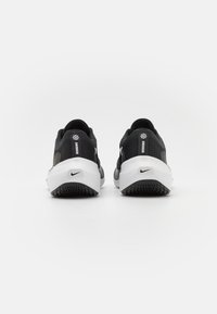 Baskets noires et blanches avec une tige texturée, une semelle courbée et un logo Nike bien visible sur le talon. Semelle extérieure en caoutchouc avec des détails de traction.