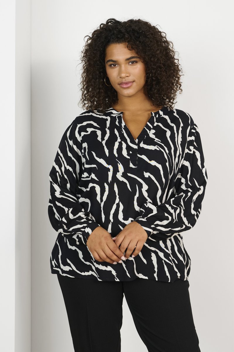 Haut à motifs noir et blanc avec une coupe ample, des manches longues et un col en V. Le tissu semble lisse et léger.