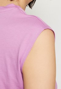 Košile s krátkým rukávem z světle růžové bavlny, s kulatým výstřihem a jednoduchým designem. Ukazuje rameno a strukturu látky.