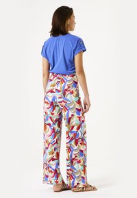 Blaues Kurzarmoberteil kombiniert mit bunten, gemusterten weitgeschnittenen Hosen mit abstrakten Design in Rot, Pink, Blau und Creme.