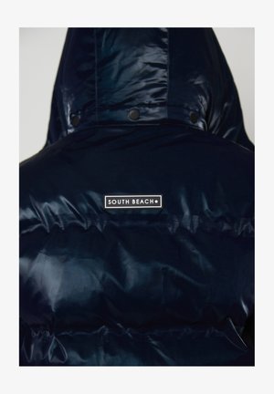 Ciemnoniebieska, błyszcząca kurtka puchowa z kapturem, z naszywką "South Beach" na górnej części pleców.