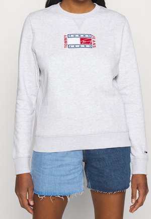 Grå sweatshirt med rund hals, ribbade ärmslut och nederkant. Försedd med broderad "TOMMY JEANS"-logotyp i röd och blå framtill.