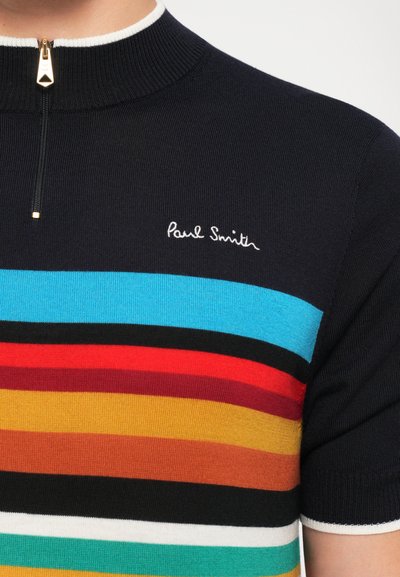 Lyhythihainen, vetoketjullinen polo-paita tummansinisenä, jossa on monivärisiä vaakasuoria raitoja. Varustettu kultaisella vetoketjulla ja valkoisella kauluksen reunan viimeistelyllä. Brodeerattu logo.