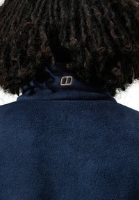 Marineblaue Fleecejacke mit hohem Kragen und kleinem Logo in goldener Stickerei auf der Rückseite. Weiche Textur mit glatter Oberfläche.