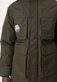 Veste vert foncé avec quatre grandes poches avant à rabat et un logo rond blanc Jack & Jones sur la poche supérieure gauche.