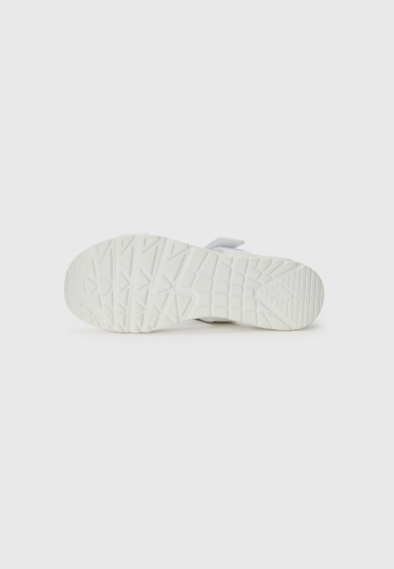 Suela de zapatilla blanca con goma texturizada para agarre, que presenta un patrón de banda de rodadura distintivo y un upper suave y flexible en gris claro.