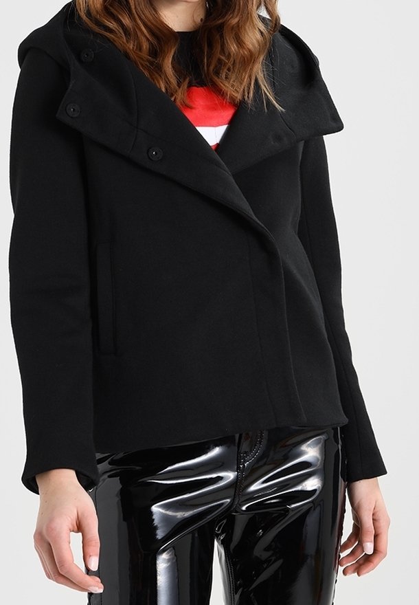 Sort dobbeltradet jakke med en stor hætte, som har en glat overflade og forlommer, parret med blanke sorte bukser.