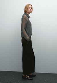 Gray knitted sweater with a high collar and sheer sleeves, paired with black wide-leg trousers and flat shoes with a circular buckle.