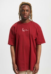 Rød bomulds t-shirt med korte ærmer, rund hals og et hvidt kursiv logo på brystet. Løs pasform og glat tekstur.
