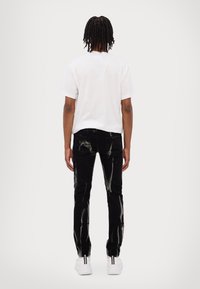 Vit kortärmad t-shirt och svarta jeans med slitna detaljer, med ljusa färgsplatter och slim fit, matchat med vita sneakers.