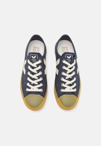 Navy denim sneakers with white leather accents, beige laces, and a green rubber toe cap. Flat design with a gum rubber sole.