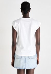 Hvid bomulds t-shirt med korte ærmer, vist fra ryggen, parret med en lys denimnederdel og med et lige snit.