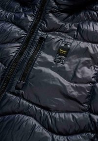 Primo piano di una giacca a piumino nera lucida con una tasca con cerniera e una piccola toppa con la scritta "Blauer U.S.A."