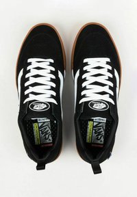 Scarpe da skate nere in suede con lacci bianchi e strisce laterali, dotate di una suola in gomma e solette etichettate, progettate per comfort e aderenza.