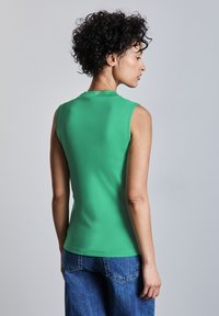 Top verde senza maniche in un tessuto liscio, design aderente, con scollatura tonda. Abbinato a jeans a gamba larga in denim blu.