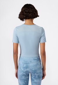 Jasnoniebieski sportowy crop top z krótkimi rękawami i siateczkowym detalem na plecach. Połączony z jasnoniebieskimi legginsami w wzory z logo.