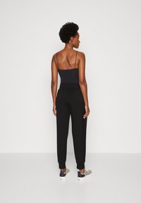 Melnas bezpiedurkņu blūze ar plānām siksnām, apvienota ar melnām sporta biksēm ar piegrieztiem potīšu galiem un zīmējumu sporta apaviem melnā, baltā un zelta akcentiem.