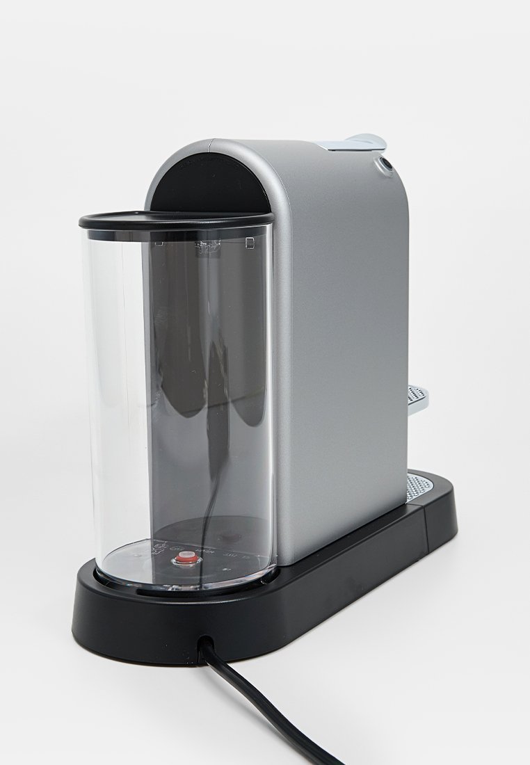 Appareil de comptoir argenté avec un conteneur transparent, base noire et bouton d'alimentation rouge. Il présente un design élégant et moderne.