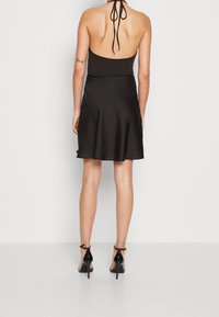 Svart halterneck-klänning i slät tyg, med en utsvängd kjol och en rygg med knytband. Matchas med svarta högklackade sandaler.