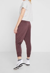 Graues, kurzärmeliges Cropped-T-Shirt kombiniert mit kastanienbraunen, taillierten Sweatpants mit einem gedrehten Design und elastischen Bündchen. Weiße Sneakers mit schwarzen Akzenten.