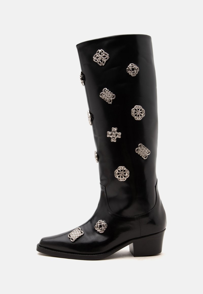 Botte noire en cuir jusqu’au genou avec un petit talon, ornée de multiples décorations en nœud celtique argenté sur la tige et le pied.