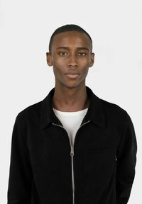 Svart hettejakke med spredt krage og frontlomme, lagd over en hvit t-skjorte med rund hals. Glatt tekstur, minimalistisk design.