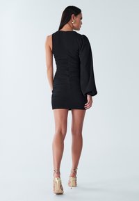 Melnas mini kleita ar asimetriskām piedurknēm, ručēta detalizācija un pieguļošs siluets. Valota ar zelta krāsas siksniņām apvilktām kurpēm ar papēžiem.