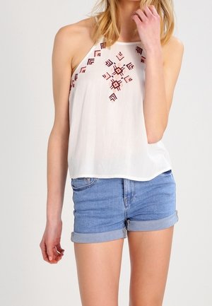 Witte mouwloze top met rode geometrische borduursels, gecombineerd met opgerolde denimshorts. Heeft een lichtgewicht, gestructureerde stof.