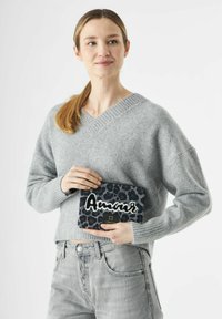 Zwarte en grijze luipaardprint clutch met witte "Amour" borduursel, ritssluiting en gouden hardware, vastgehouden door een persoon in een grijze trui.