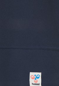 Námořnická modrá texturovaná látka s mřížkovým vzorem. Na dolním pravém rohu se nachází bílá etiketa s barevným logem.