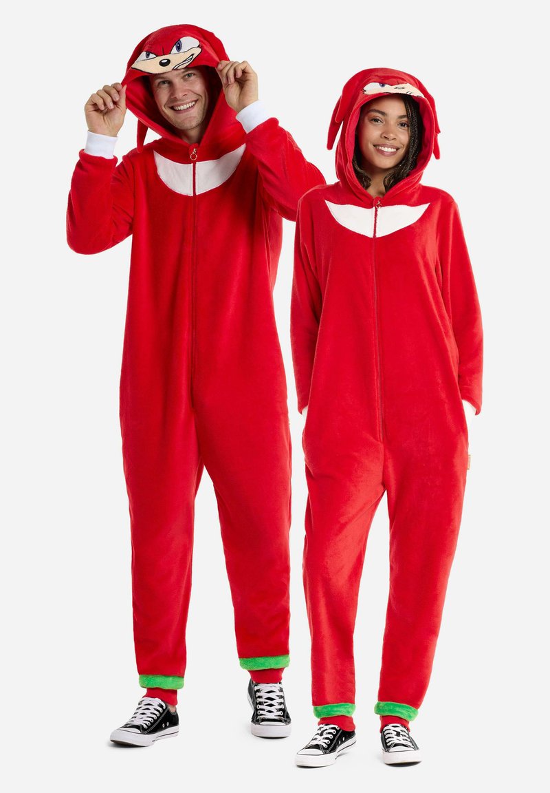 Red fleece onesies with hoods, featuring a character face and white accents. Cuffs and leg hems have green trim. Black sneakers worn.