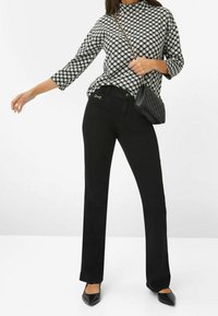 Pantaloni neri a gamba dritta con un'accento in hardware dorato lucido, abbinati a una camicia a maniche lunghe a quadri bianca e nera. Borsa nera semplice e tacchi.