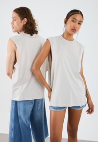 Svetlošedý bezrukávový top s voľným strihom, jemným materiálom a spadnutými ramienkami, vystavený dvoma modelkami zozadu a zpredu.