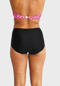 Svarta höga bikiniunderdelar i kombination med en rosa blommig bandeau-top med spänne, som visar en slät textur.