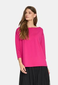 Długorękawowy top w kolorze fuksji z szerokim dekoltem i luźnym krojem, w połączeniu z czarną spódnicą z tiulu, charakteryzującą się gładką fakturą tkaniny.