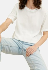 Bílá tričko s krátkým rukávem a kulatým výstřihem, vyrobené z hladké tkaniny, v kombinaci se světle modrými džínami s volným střihem.