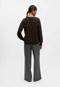 Pull en tricot texturé marron avec des manches longues, associé à un pantalon large gris. La tenue présente une coupe décontractée et des accents côtelés.