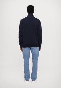 Sudadera navy con cuello alto, cremallera frontal y puños acanalados, combinada con jeans de color azul claro. Diseño sencillo, tela suave.
