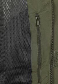 Donkergroene en zwarte zipvest met een meshstructuur en gladde stof, voorzien van een zijzak en een klittenbandpatch aan de rechterkant.