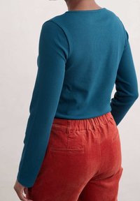 Lange mouwen, geribbelde teal top in combinatie met oranje corduroy broek. De top heeft een ronde halslijn; de broek heeft een elastische tailleband en achterzakken.