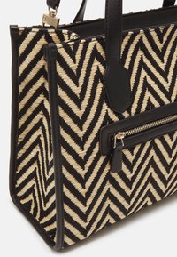 Sort og creme chevron-mønstrede taske med en struktureret form, læderdetaljer og en lynlåslomme. Tekstureret materiale med solide håndtag.