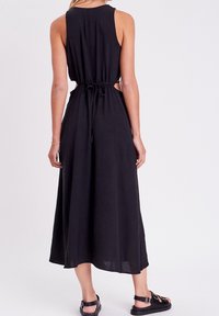 Robe maxi noire sans manches avec un dos nu, lien ajustable à la taille, en tissu léger, avec une texture lisse.