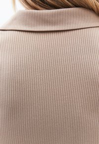 Tessuto a coste beige, dettaglio del colletto visibile, superficie testurizzata con strette righe verticali. Il materiale appare morbido e leggero.