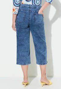 Džínové culottes ve středně modré barvě s širokým střihem, středním vzestupem a dvěma zadními kapsami. Lem je zakončen vyšitým lemem.